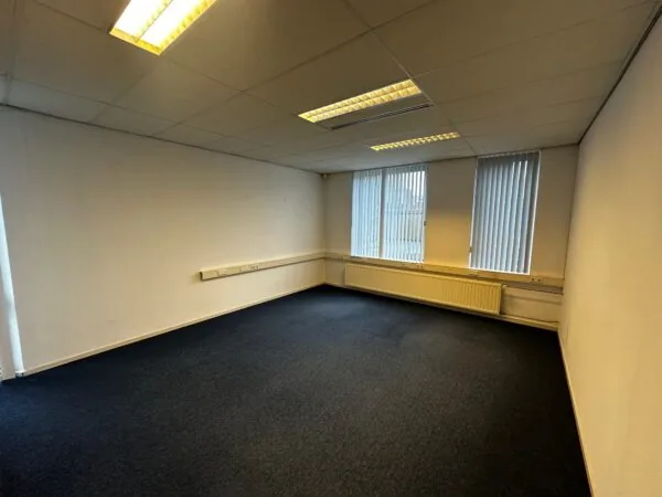 Leeg kantoor met tapijtvloer, systeemplafond en grote ramen met verticale jaloezieën aan de Van Bleyswijckstraat.